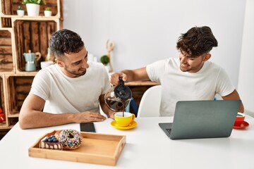 Two hispanic men couple pouring coffee having breakfast at home