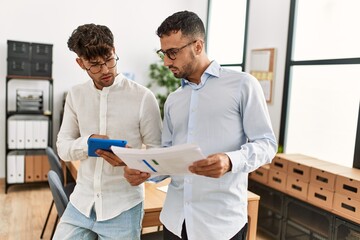 Two hispanic men business workers using touchpad reading documents working at office