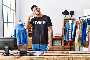 Young hispanic man working at retail boutique smiling doing phone gesture with hand and fingers like talking on the telephone. communicating concepts.