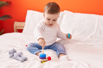 Adorable caucasian baby playing with toys sitting on bed at bedroom