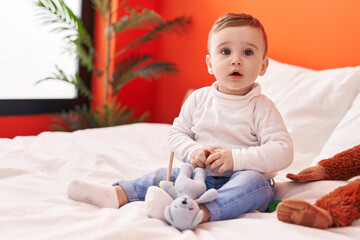Adorable caucasian baby playing with toys sitting on bed at bedroom