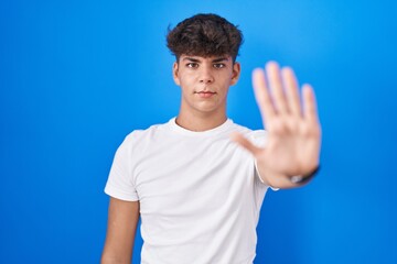 Hispanic teenager standing over blue background doing stop sing with palm of the hand. warning...