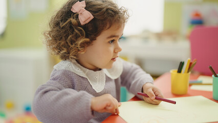 Adorable hispanic girl preschool student sitting on table drawing on paper at kindergarten