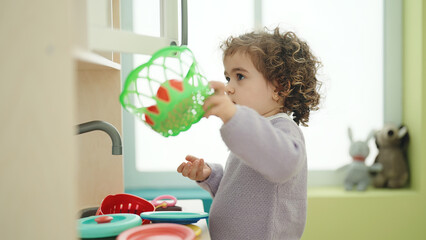 Adorable hispanic girl playing with play kitchen standing at kindergarten