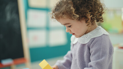 Adorable hispanic girl playing with construction blocks standing at kindergarten