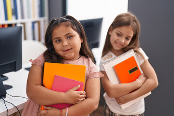 Two kids students smiling confident holding books at classroom