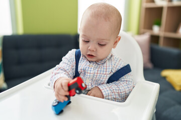 Adorable caucasian baby palying with cars toy sitting on highchair at home