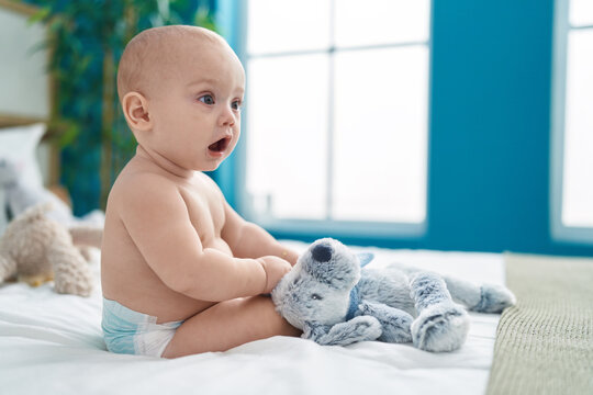 Adorable caucasian baby sitting on bed with relaxed expression at bedroom
