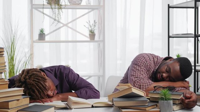 Exhausted education. Sleeping men. Preparing exam. Tired male students laying desk on pile books in light room interior.