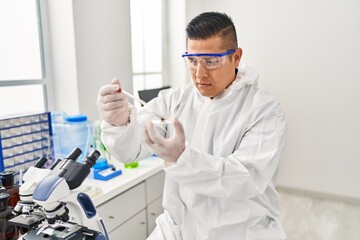 Young latin man scientist pouring liquid on cannabis herb sample at laboratory