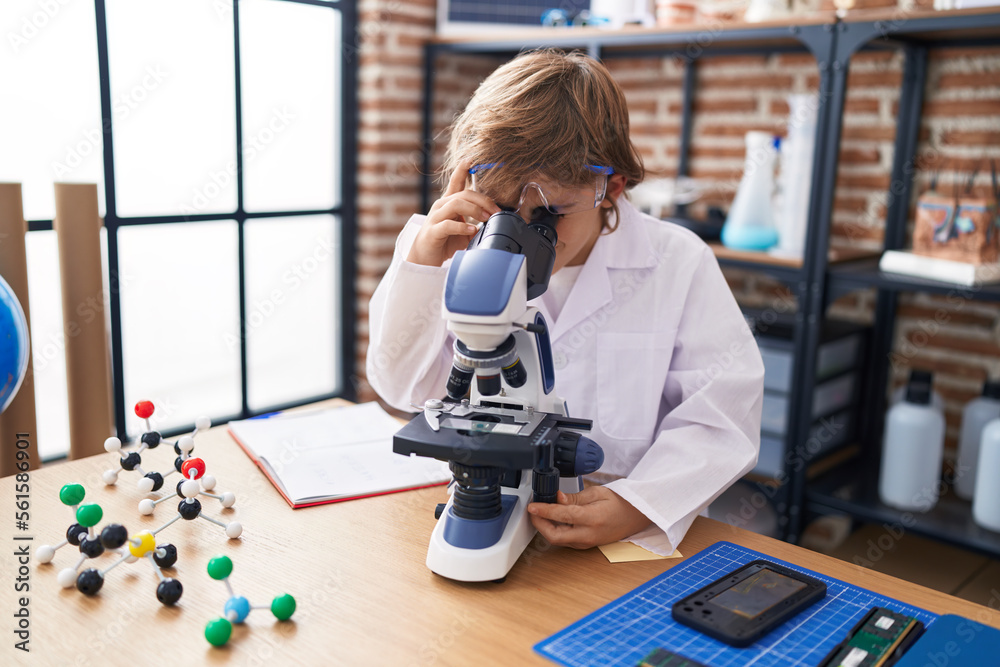 Poster Adorable caucasian boy student using microscope at classroom