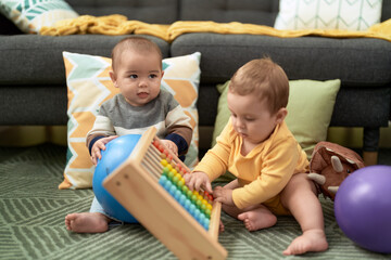 Two toddlers playing with balls and abacus sitting on floor at home