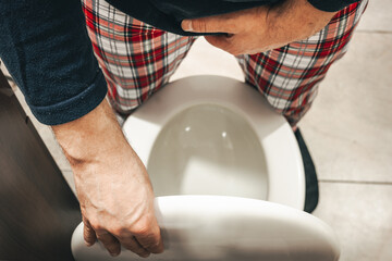 Fototapeta na wymiar Urination problem, A man in pajamas in the toilet squeezes his crotch and lifts the toilet seat, Health concept, Male prostate problem, urinary system function, bladder pain