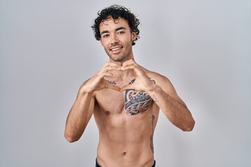 Hispanic man standing shirtless smiling in love doing heart symbol shape with hands. romantic concept.