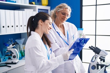 Two women scientists writing on document holding test tubes at laboratory