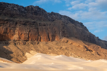 First light hits a rocky cliff above a sand dune