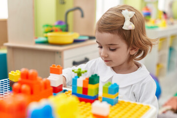 Adorable caucasian girl playing with construction blocks sitting on table at kindergarten