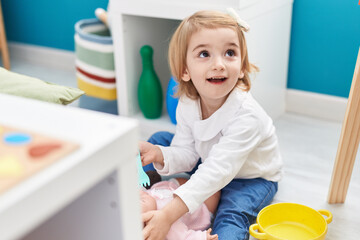 Adorable caucasian girl playing with baby doll sitting on floor at kindergarten