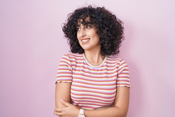 Young middle east woman standing over pink background smiling looking to the side and staring away thinking.