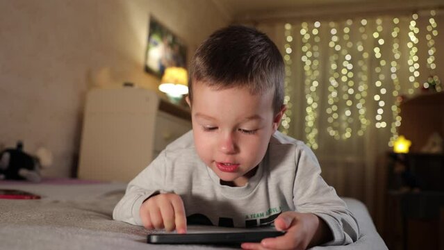 Cute Little Boy Uses Phone At Home in Room. Kid Plays Mobile Games On Smartphone Smiling and Showing Emotions
