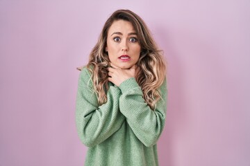 Fototapeta premium Young caucasian woman standing over pink background shouting and suffocate because painful strangle. health problem. asphyxiate and suicide concept.