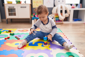 Adorable caucasian boy playing with hoops toy sitting on floor at kindergarten