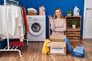 Hispanic woman putting clothes in donation box smiling with happy face winking at the camera doing...