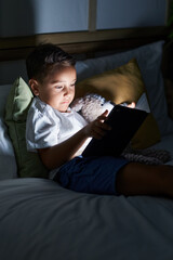 Adorable hispanic toddler using touchpad lying on bed at bedroom