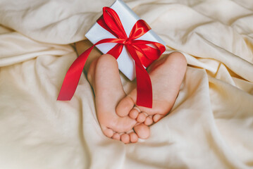 Children's feet and heels with heart, gift on a white bed to Christmas, Valentine's day, Mother's Day. Infant baby is sleeping in his crib. Importance of sleep for babies. Sleep mode babies 3 y.o.
