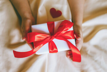 Children's hand with gift on a white bed to Christmas, Valentine's day, Mother's Day.
