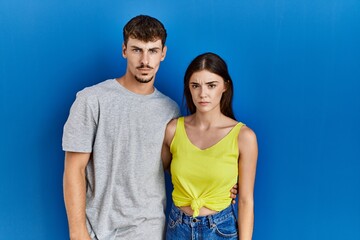 Fototapeta premium Young hispanic couple standing together over blue background skeptic and nervous, frowning upset because of problem. negative person.