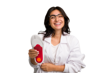 Young indian chiropodist woman holding a insoles for shoes cut out isolated laughing and having fun.