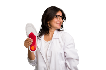 Young indian chiropodist woman holding a insoles for shoes cut out isolated looks aside smiling, cheerful and pleasant.