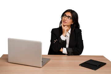 Young indian woman in a table with a laptop and tablet isolated looking sideways with doubtful and skeptical expression.