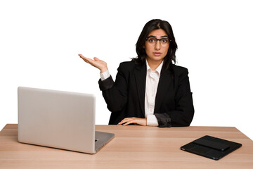 Young indian woman in a table with a laptop and tablet isolated impressed holding copy space on palm.