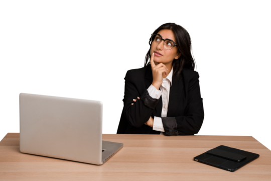 Young indian woman in a table with a laptop and tablet isolated looking sideways with doubtful and skeptical expression.
