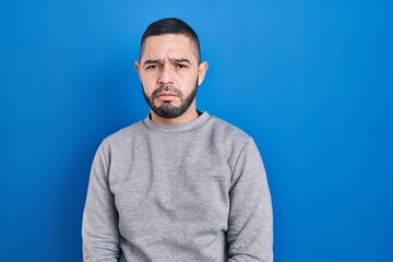 Hispanic man standing over blue background depressed and worry for distress, crying angry and...
