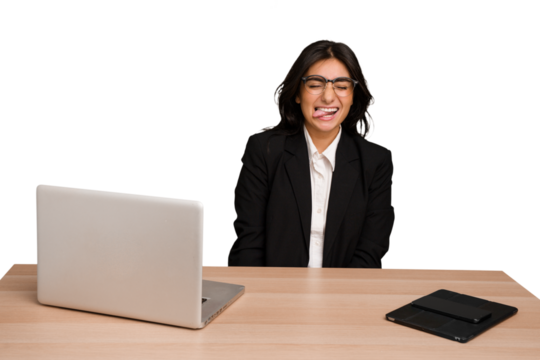 Young indian woman in a table with a laptop and tablet isolated funny and friendly sticking out tongue.