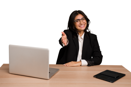 Young indian woman in a table with a laptop and tablet isolated stretching hand at camera in greeting gesture.