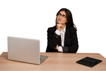 Young indian woman in a table with a laptop and tablet isolated thinking and looking up, being reflective, contemplating, having a fantasy.