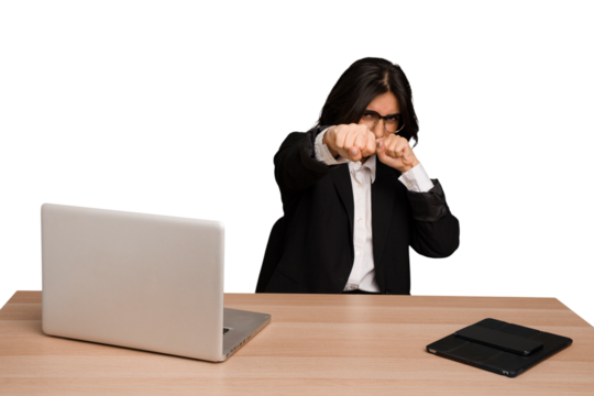 Young indian woman in a table with a laptop and tablet isolated throwing a punch, anger, fighting due to an argument, boxing.
