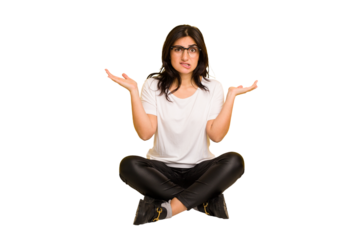 Young indian woman sitting on the floor cut out isolated confused and doubtful shrugging shoulders to hold a copy space.