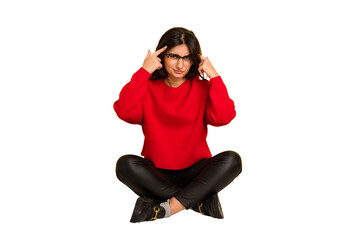 Young indian woman sitting on the floor cut out isolated focused on a task, keeping forefingers pointing head.