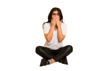 Young indian woman sitting on the floor cut out isolated shocked, covering mouth with hands, anxious to discover something new.