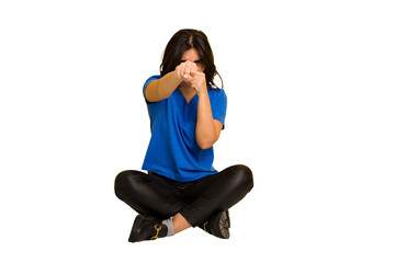 Young indian woman sitting on the floor cut out isolated throwing a punch, anger, fighting due to an argument, boxing.