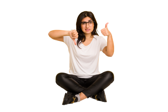 Young indian woman sitting on the floor cut out isolated showing thumbs up and thumbs down, difficult choose concept