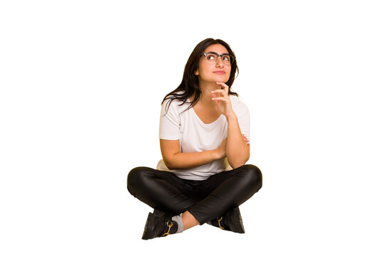 Young indian woman sitting on the floor cut out isolated thinking and looking up, being reflective, contemplating, having a fantasy.