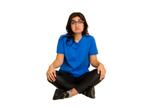Young indian woman sitting on the floor cut out isolated shrugs shoulders and open eyes confused.