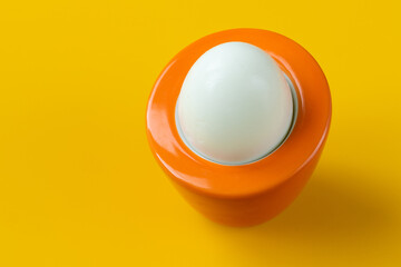 boiled egg in an orange stand on a yellow background, original design, the concept of reviving, valuable nutrients, protein and vitamins