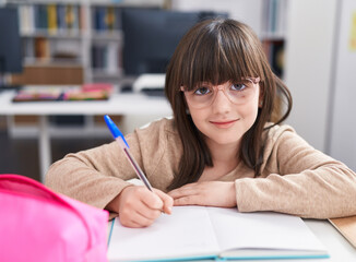 Adorable hispanic girl student sitting on table doing homework at classroom